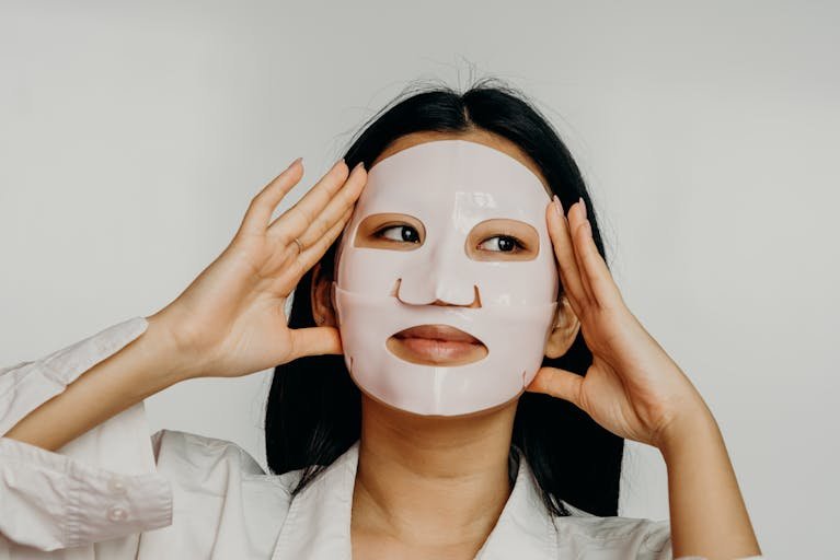 Asian woman applying hydrating sheet mask as part of her skincare routine.